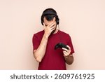 Man playing with a video game controller over isolated wall with tired and sick expression