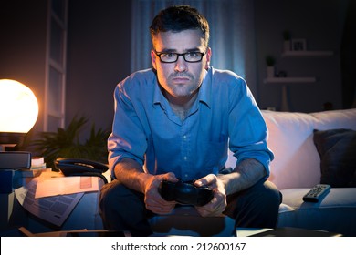 Man Playing Videogames Late At Night In A Messy Living Room, Sitting On Sofa.