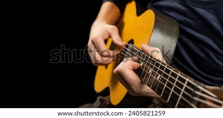 Man plays an acoustic guitar on a black background. The musician clamps the frets of the guitar on the neck. Musical instrument. Soft focus. Place for text. Copy space.