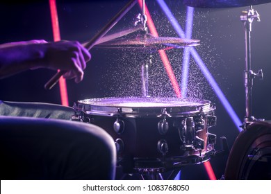 the man plays the drums, the game is on the working drum with sticks close-up. On the background of colored lights with splashes of water. Musical concept with a working drum.