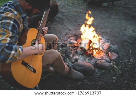 man plays the guitar by the fire in nature. summer camping. relaxation in nature