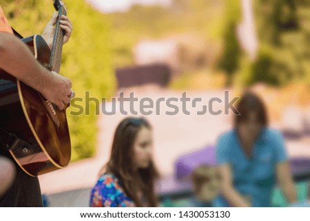 A man plays the guitar for children and their parents on vacation.Shallow depth of field. Focus on guitar
