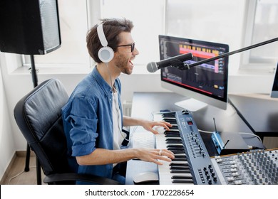 Man Plays Guitar And Singing And Produce Electronic Soundtrack Or Track In Project At Home. Male Music Arranger Composing Song On Midi Piano And Audio Equipment In Digital Recording Studio