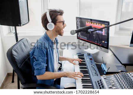 Man plays guitar and singing and produce electronic soundtrack or track in project at home. Male music arranger composing song on midi piano and audio equipment in digital recording studio