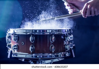 man plays musical percussion instrument with sticks closeup on a black background, a musical concept with the working drum, beautiful lighting on the stage
