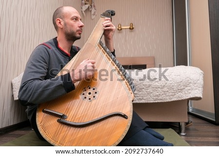 A man plays a traditional Ukrainian instrument at home. The musician plays the bandura in his apartment.