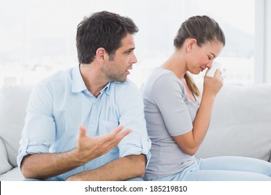 Man Pleading With His Crying Partner On The Couch At Home In The Living Room