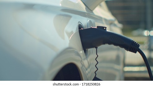 Man Plugging In Electric Car At Home At Electro Charging Station. Luxury White Electrical Car Recharging. Environmentally Conscious Man Charging His Electric Vehicle.