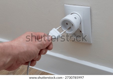 A man plugs a plug into a socket, a man's hand inserting a plug into the holes of a smart socket, an electrical outlet controlled by a phone, a smart electrical outlet, an electrical outlet on a white wall in a room