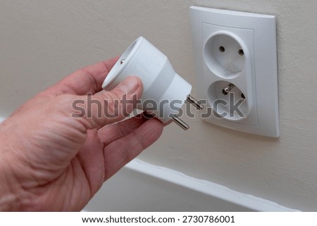A man plugs a plug into a socket, a man's hand inserting a plug into the holes of a smart socket, an electrical outlet controlled by a phone, a smart electrical outlet, an electrical outlet on a white wall in a room