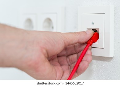 Man Plugs Red Network Cable In Wall Outlet For Office Or Private Home Lan Ethernet Connection With Power Outlets Flat View On White Plaster Wall Background - Selective Focus