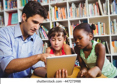 Man pointing a digital tablet to two children a library - Powered by Shutterstock