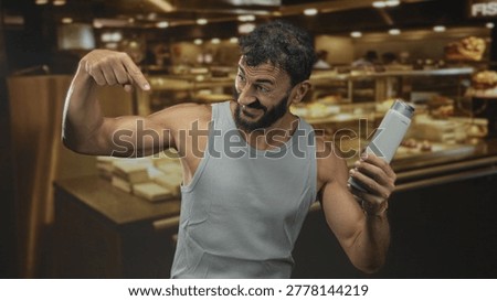 Man pointing finger to armpit while holding shampoo bottle inside building bakery counter, visible armpit and smiling face; personal care confidence.