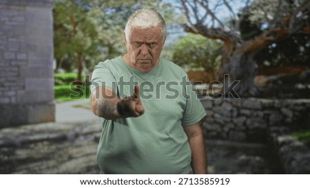 Man pointing finger at camera in front of stone wall building, stern frown and direct gesture toward viewer; anger warning.