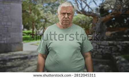 Man pointing finger at camera in front of stone wall building, stern frown and direct gesture toward viewer; anger warning.