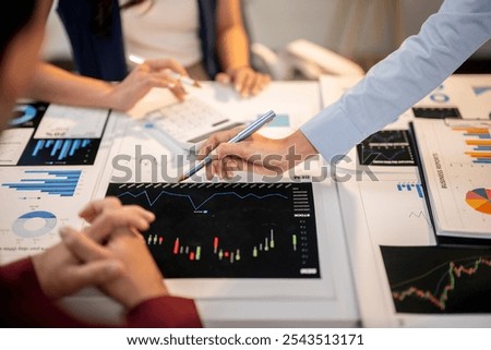 A man is pointing at a graph on a table while two other people look on. The graph shows a downward trend, which could indicate a negative outcome. Scene is serious and focused