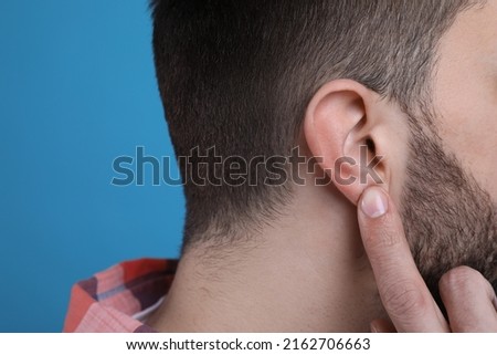 Man pointing at his ear on light blue background, closeup