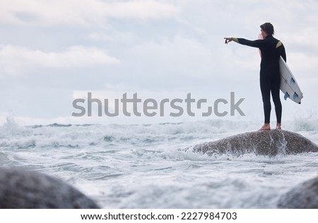 Man, pointing or surfer on rocks at beach, ocean or rough sea and watching tide, waves or water movement in Hawaii. Sports athlete, surf board or surfing person in fitness, workout or nature training