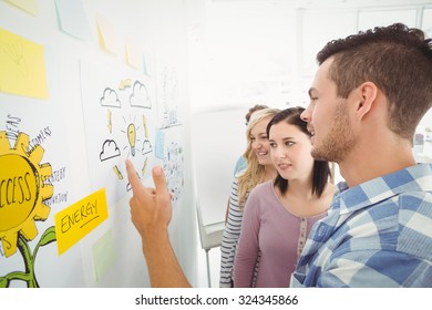 Man pointing at wall with sticky notes and drawings while standing in creative office - Shutterstock ID 324345866