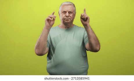 Man points finger at camera while holding v with hand over his eye, wearing green shirt in a studio setting; confidence attention.