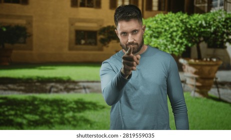 Man points finger directly at camera, visible beard and hand, standing before building courtyard and planter; confidence challenge.