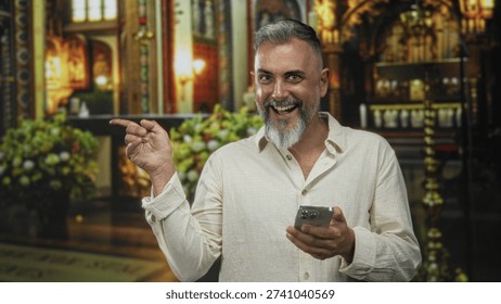 Man points finger at smartphone while laughing and holding phone in right hand inside ornate catholic church building with altar behind him; joy faith connection.