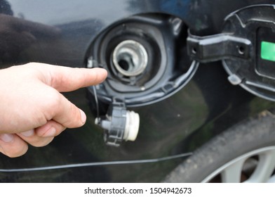 A Man Points To The Gas Tank Of A Car. The Gas Tank Of A Black Car Is Open For Refueling.