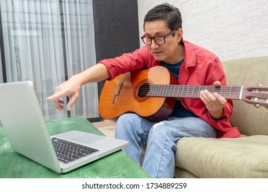 Man Points To His Laptop Monitor In A Virtual Guitar Class At Home