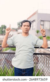 A man points upwards with both hands, set against the backdrop of an urban scene with a neutral color palette indicating a thoughtful or perhaps instructive moment.