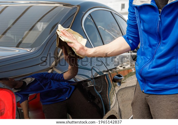 man polishes the car, uses a\
microfiber cloth and polish to wipe the car\'s body with\
polish.