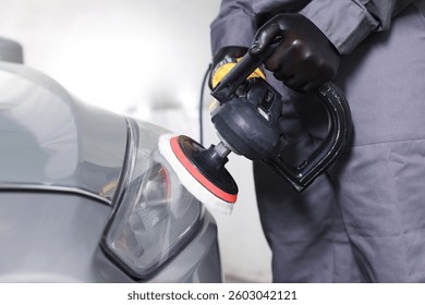 Man polishing car headlight with orbital polisher indoors, closeup