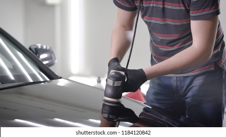 man is polishing surface of hood of black automobile in auto-service, using electric grinding machine, processing car by protective layer - Powered by Shutterstock