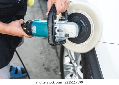 A Man Polishing The Surface Of A White Sedan With An Electric Buffing Machine. At An Auto Detailing Shop.