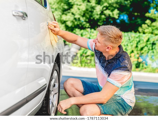 Man polishing white\
car with rug outdoors