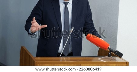 Man - politician, businessman or teacher speaks in front of microphones, leaning on podium or pulpit and gesticulating with his hands. Official press statement. Anonymous and unrecognizable. No face