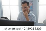 Man pondering seriously in an office setting illuminated by natural light through large windows, exuding focus and contemplation.