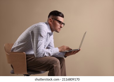 Man With Poor Posture Using Laptop While Sitting On Chair Against Beige Background