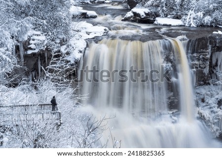 A man poses on viewing platform in front of Blackwater Falls on a winter day in Davis, West Virginia.