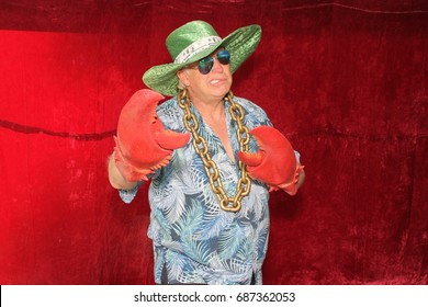 A man poses for photos in a Photo Booth. A man wears Lobster Claw Gloves and a Pimp Hat in a photo booth.