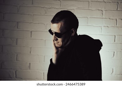 Man Posing Dramatically in Sunglasses Against White Brick Wall at Night.