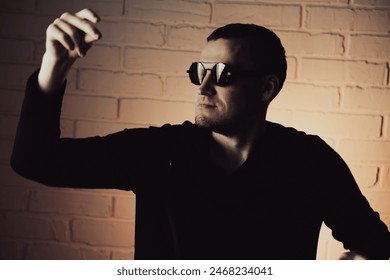 Man Posing Dramatically in Sunglasses Against White Brick Wall at Night.