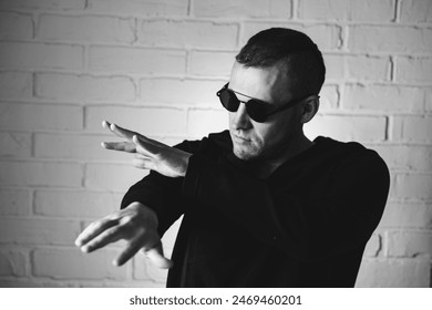 Man Posing Dramatically in Sunglasses Against White Brick Wall at Night.