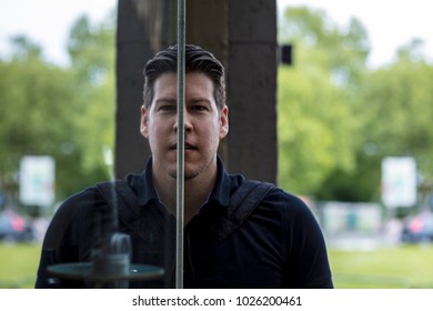 Man posing in front of glass window reflecting his image. Close up. 