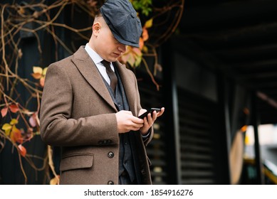 A man posing in the image of an English retro gangster of the 1920s dressed in Peaky blinders style near old brick wall.