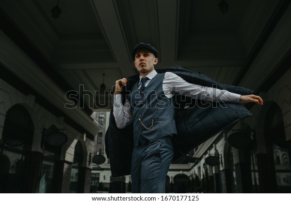 A man\
posing in the image of an English retro gangster of the 1920s\
dressed in Peaky blinders style at city\
street.