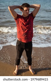 Man Posing In The Sea On A Sunny Day. Caucasian And Dark-haired. He Is Wearing A Short Sleeved T-shirt And Long Rolled Up Trousers. The Sea Is Calm. His Arms Are Behind His Head.