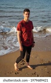 Man Posing In The Sea On A Sunny Day. Caucasian And Dark-haired. He Is Wearing A Short Sleeved T-shirt And Long Rolled Up Trousers. The Sea Is Calm. He Is Looking At The Camera.