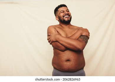 Man with pot belly embracing his natural body. Happy young man laughing cheerfully while standing shirtless against a studio background. Body positive man wearing underwear in a studio. - Shutterstock ID 2062826963