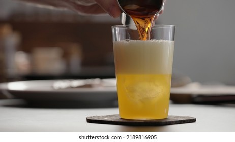 Man Pour Aperitivo In Orange Soda With Ice In Tumbler Glass To Make Spritz Drink On Concrete Countertop, Wide Photo