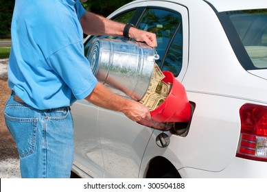 Man Pouring Bucket Of Cash Into His Gas Tank Symbolizing Economic Hardship Just To Purchase Gas And Petroleum Products. Pain At The Pump.